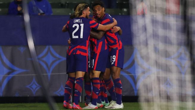 USMNT players in red and blue striped jerseys celebrate together after scoring goal against Bosnia and Herzegovina