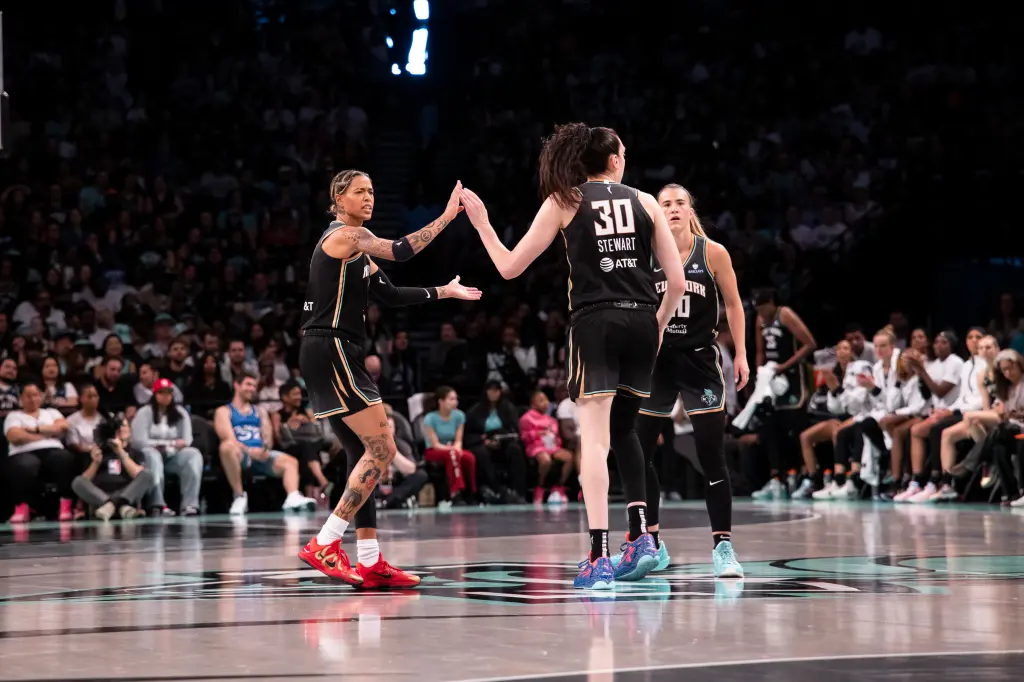 New York Liberty players celebrate during their 92-78 season opener victory over Las Vegas Aces at Barclays Center, with Breanna Stewart #30 high-fiving teammate while crowd watches in background