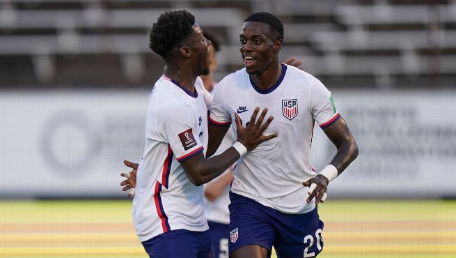 Two USMNT players in white jerseys celebrate together after scoring goal against Jamaica in World Cup qualifier