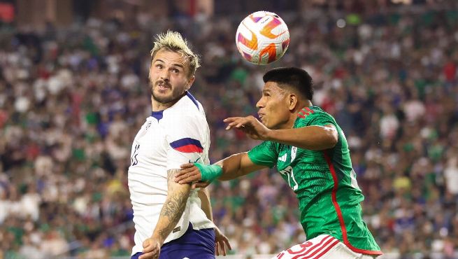 USMNT player in white jersey battles for aerial ball against Mexico player in green jersey during CONCACAF Nations League match ending in a draw.