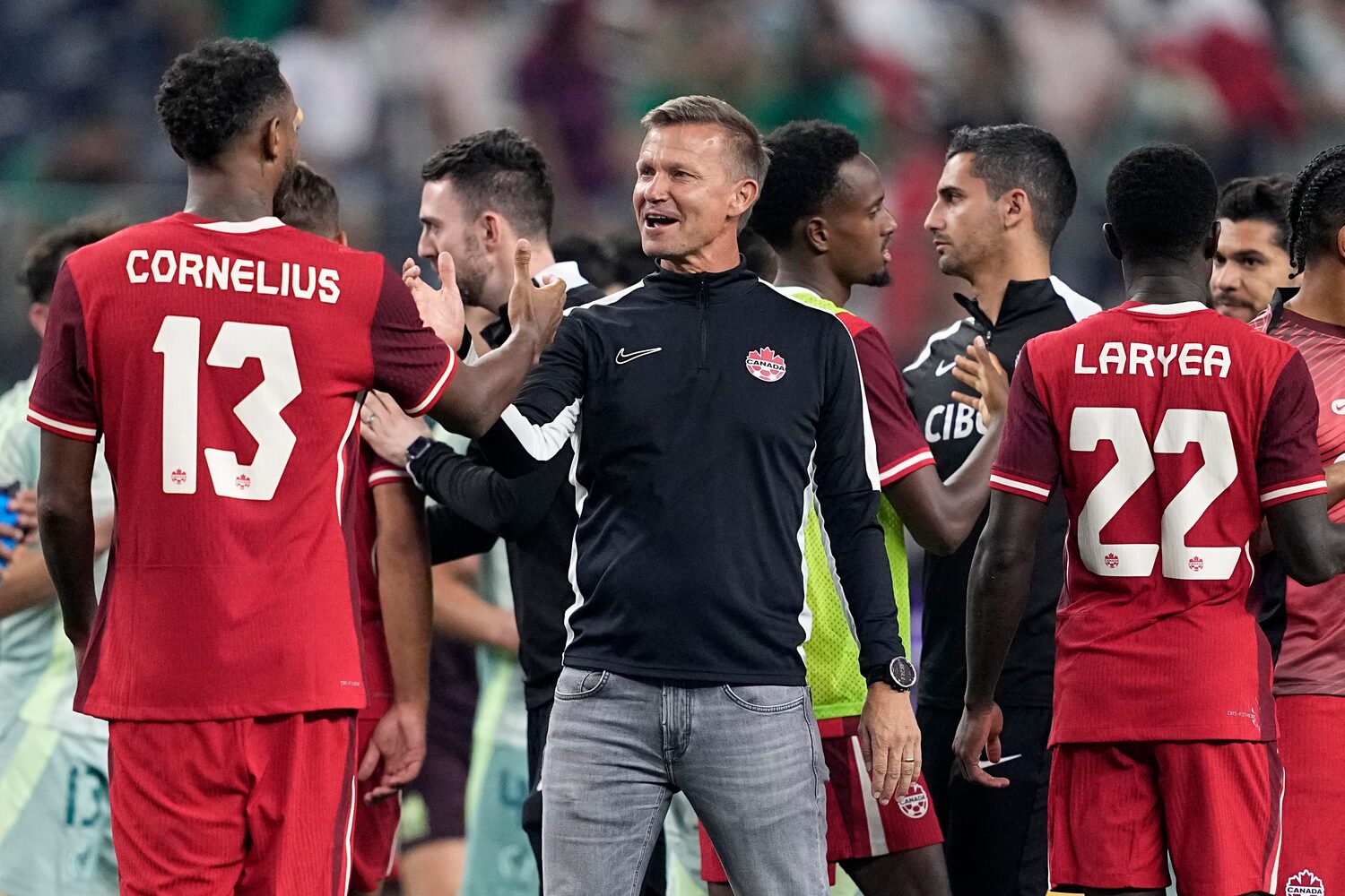 Canada head coach Jesse Marsch in black Nike jacket celebrating with his players including Derek Cornelius (#13) and Richie Laryea (#22) after their friendly match against Mexico in Arlington, Texas