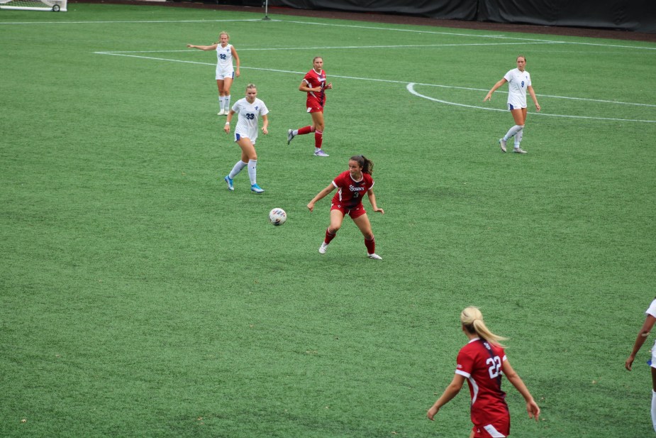 St. John's freshman Julia Lombardo in white uniform dribbles through midfield while surrounded by multiple Seton Hall players in red uniforms during women's soccer match