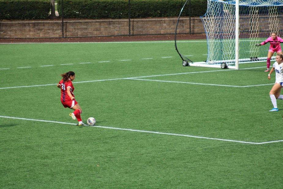 St. John's senior midfielder Emily Riggins in white uniform controls the ball in the attacking third with Seton Hall goalkeeper in pink visible in the background