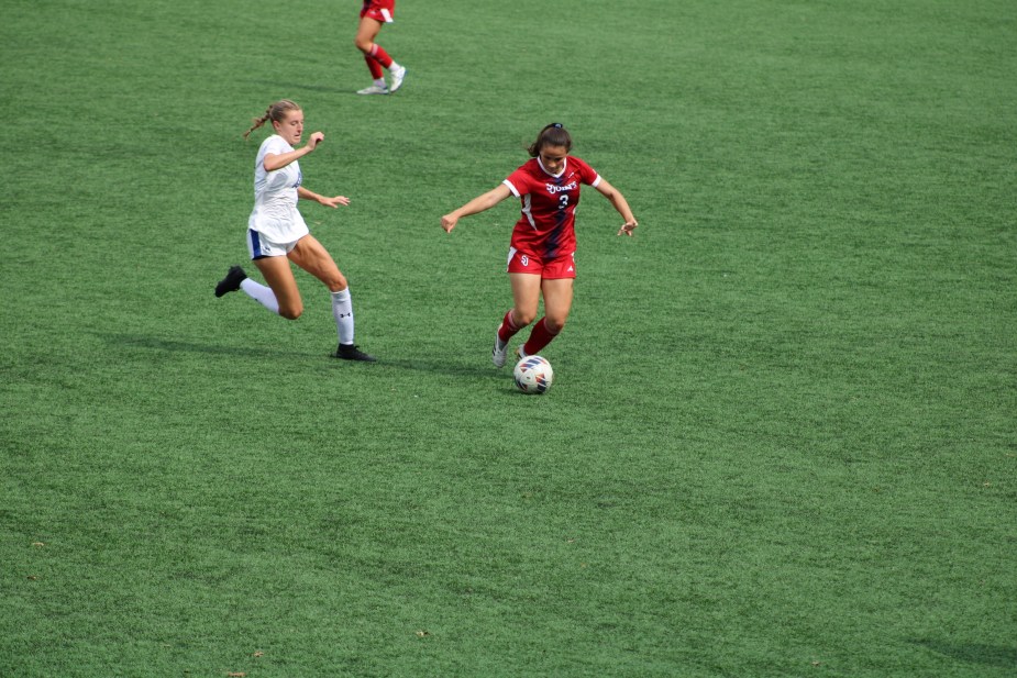 St. John's freshman midfielder Julia Lombardo in white uniform dribbles the ball while being pursued by a Seton Hall defender in red during Big East women's soccer match