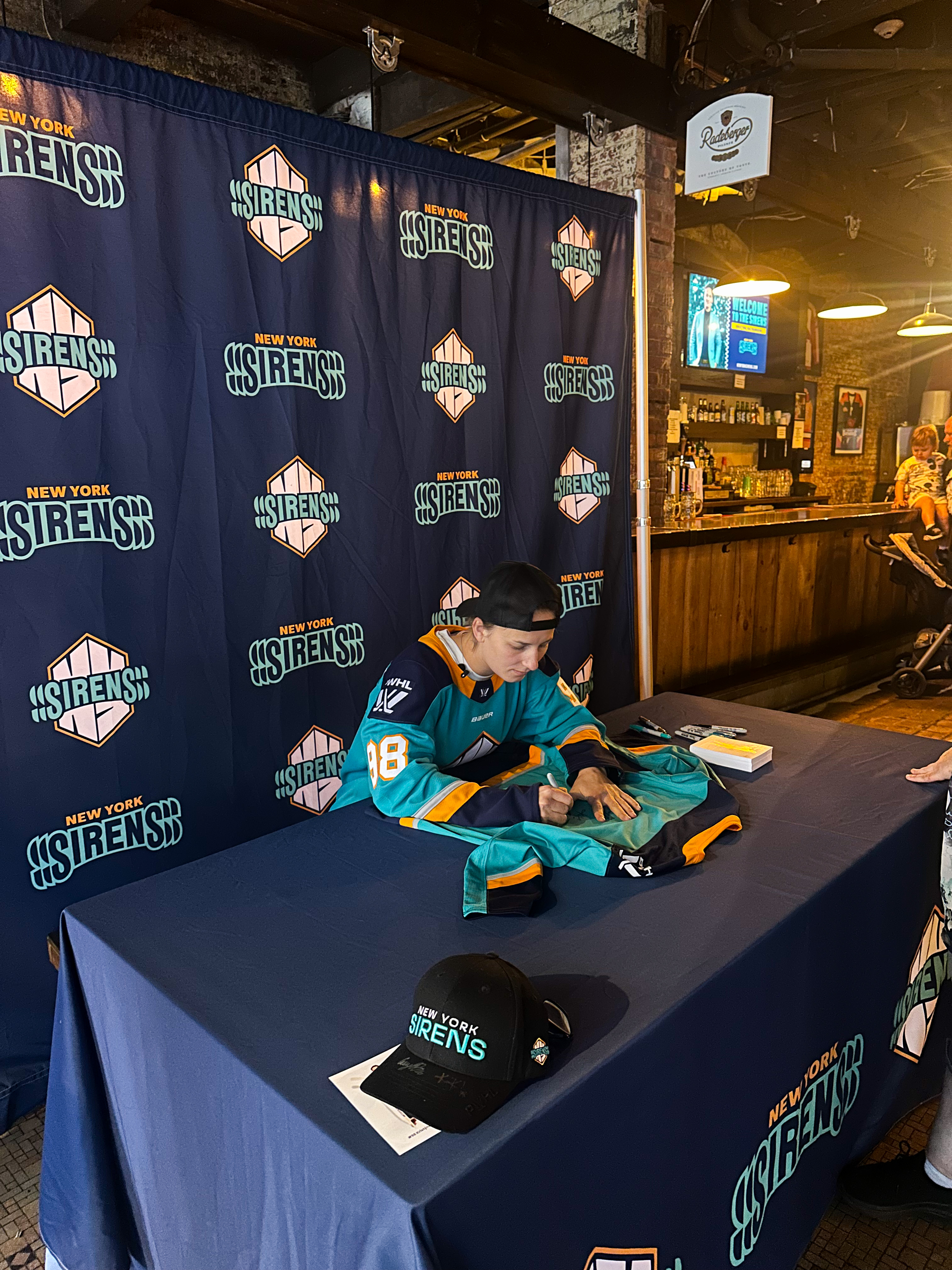 New York Sirens draft pick signing team jersey at autograph table with logo backdrop