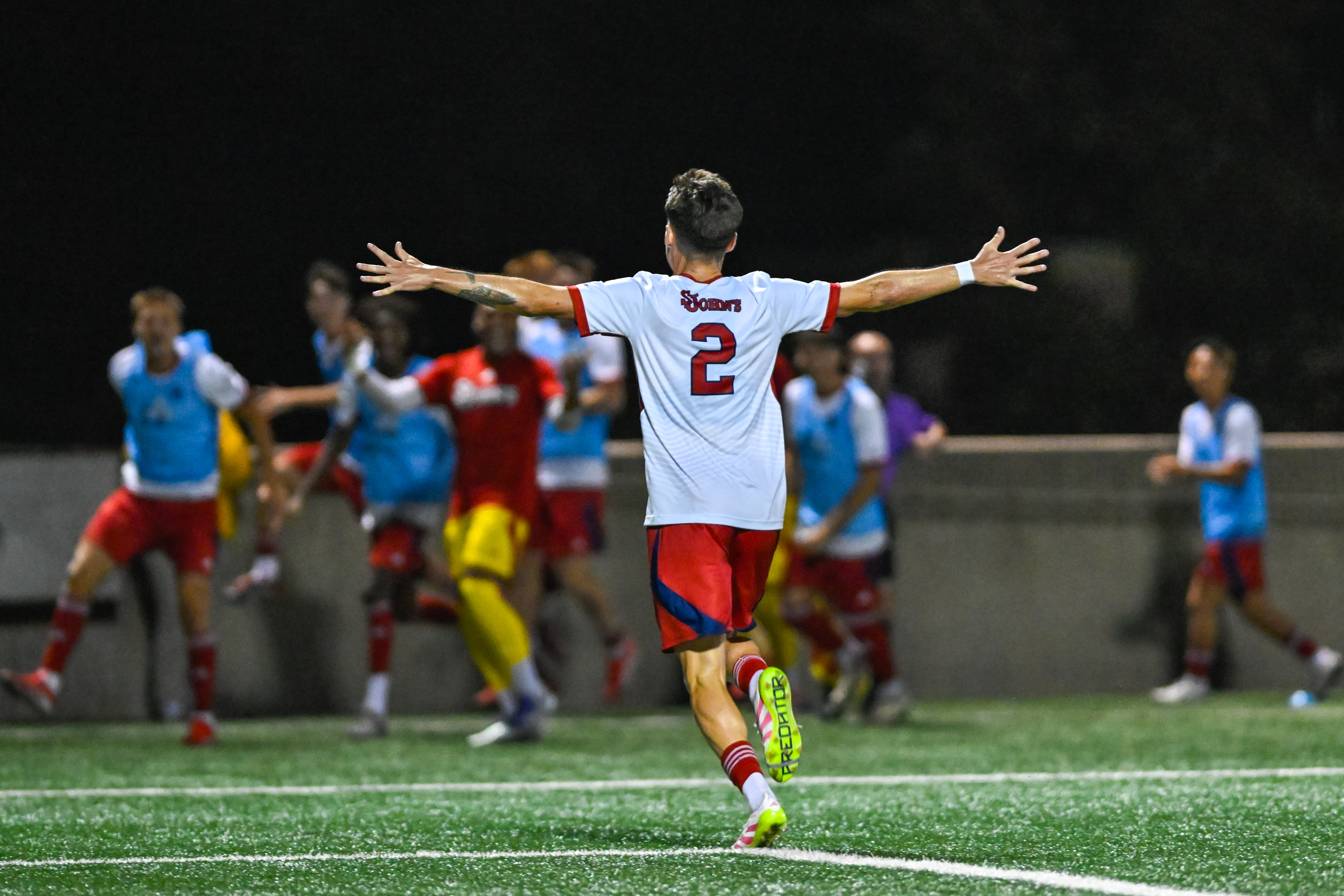 St. John's University defender Jeremy Sharp celebrating his equalizing goal with arms outstretched, wearing number 2 jersey, running toward the crowd during the historic 1-1 draw against No. 2 Marshall