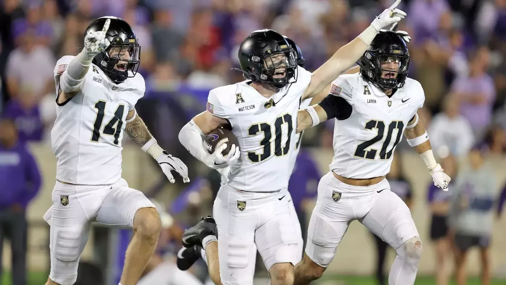 Army Black Knights safety Collin Matteson holds the football after making an interception while teammates Mitch Bolden and Tim Kloska run alongside to celebrate