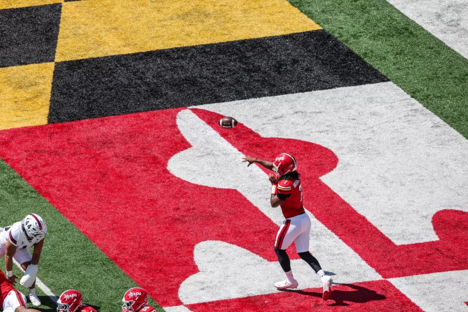 Maryland quarterback Malik Washington drops back to pass from the team's own end zone, with the Maryland state flag-inspired field design visible beneath him