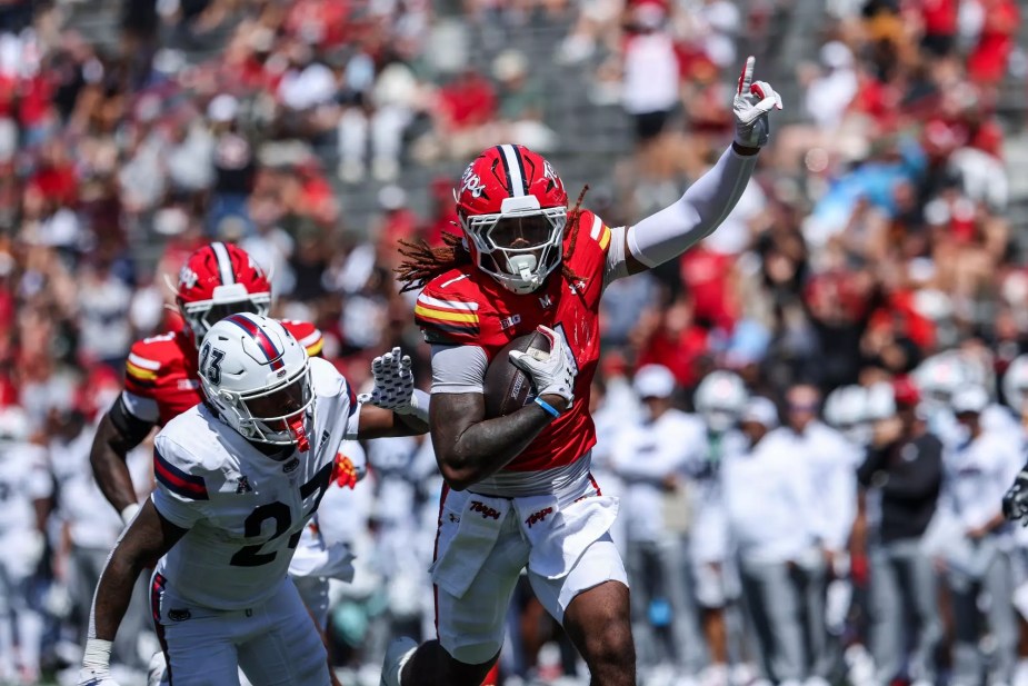 Maryland quarterback Malik Washington runs with the football while pointing upfield, evading a Florida Atlantic defender in white uniform during his touchdown run