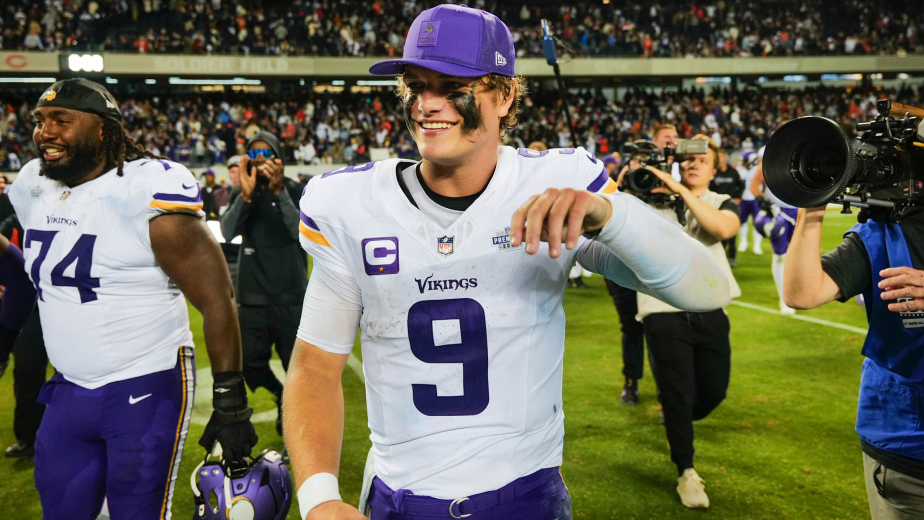 J.J. McCarthy celebrating on the field after his historic comeback win, wearing Vikings white jersey with number 9, smiling with teammates and cameras around