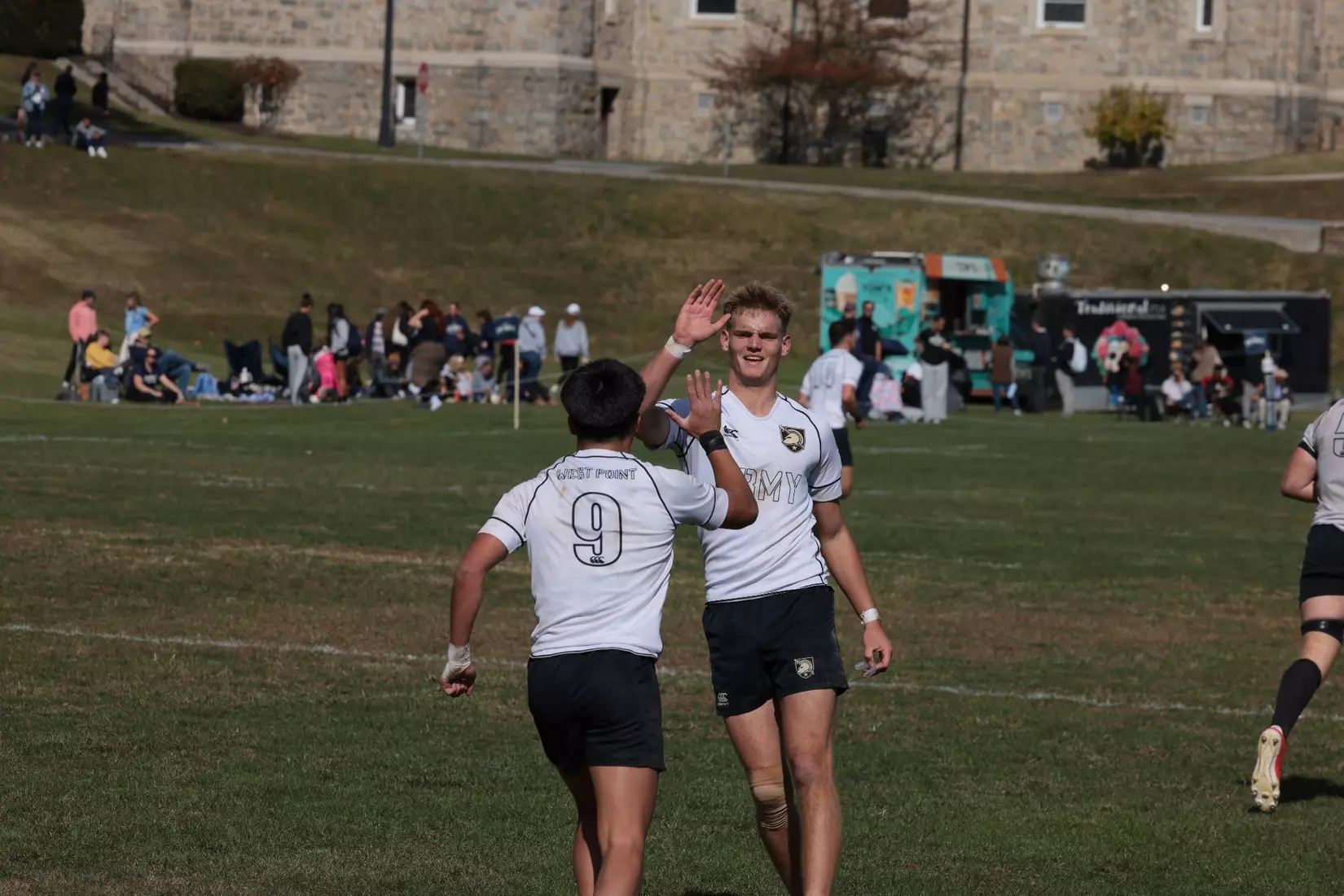 Two Army West Point men's rugby players celebrate during game action in black and gold uniforms at Anderson Rugby Complex