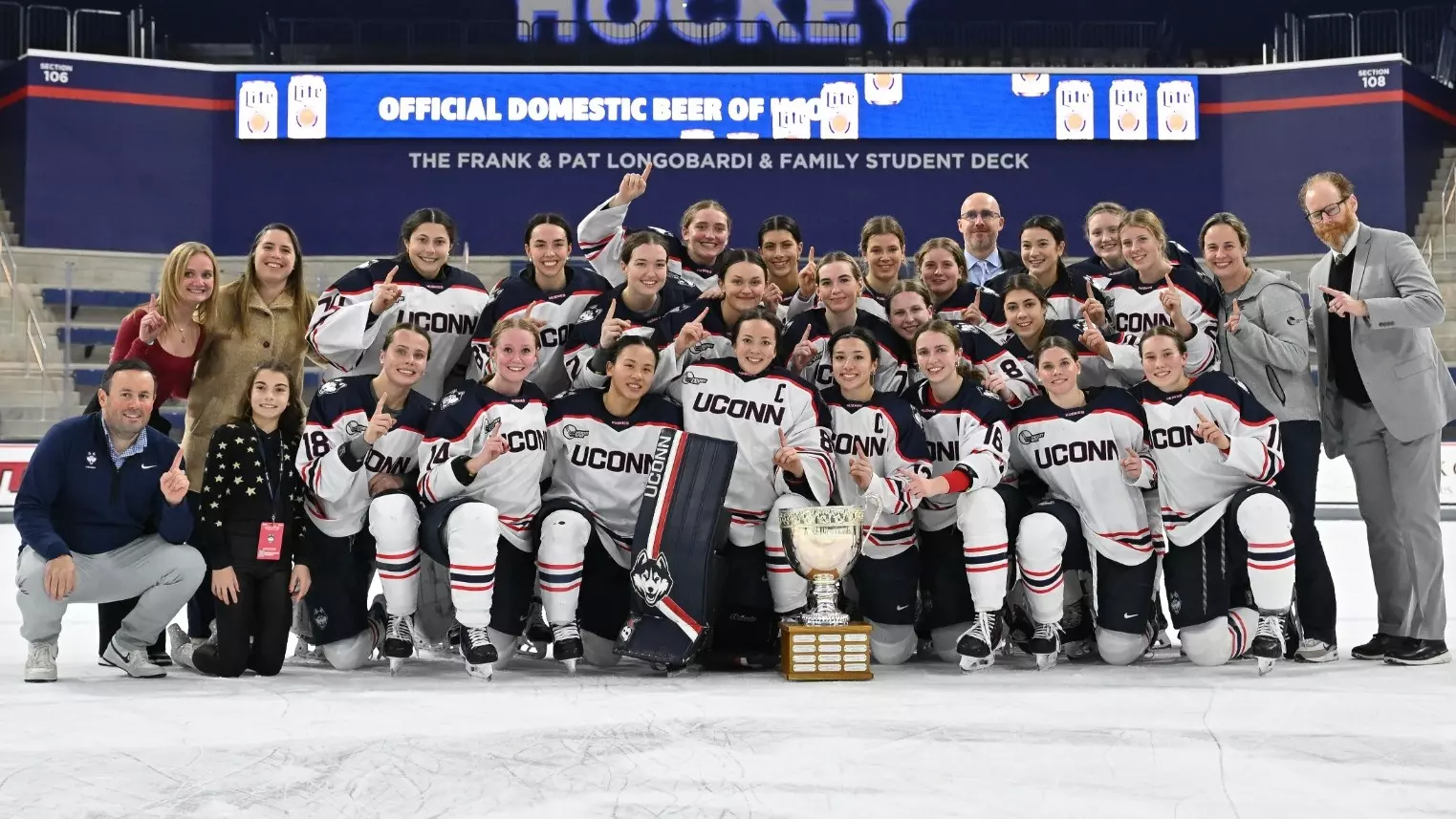 UConn women's hockey team poses with the Nutmeg Classic championship trophy at center ice at Toscano Family Ice Forum after defeating Yale 3-2 on November 29, 2025. The team celebrates in white away jerseys with the coaching staff and the championship trophy prominently displayed.