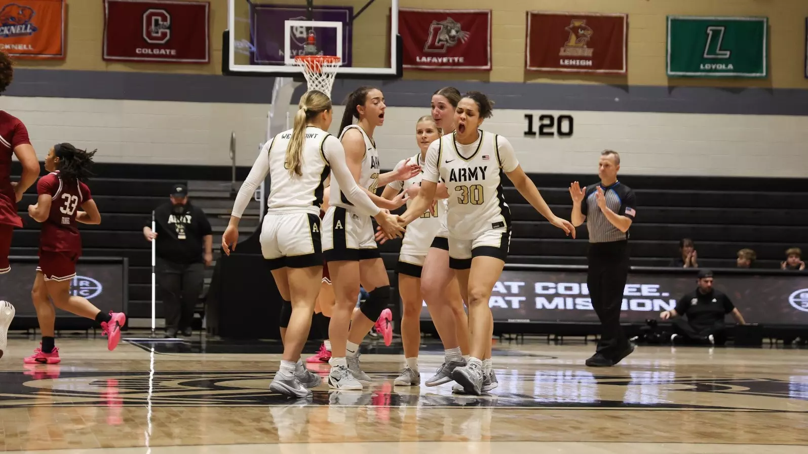 Army West Point women's basketball players celebrate together during their 64-61 victory over UMass at Christl Arena, with Kya Smith (#30) leading the huddle as teammates gather in unity on the court