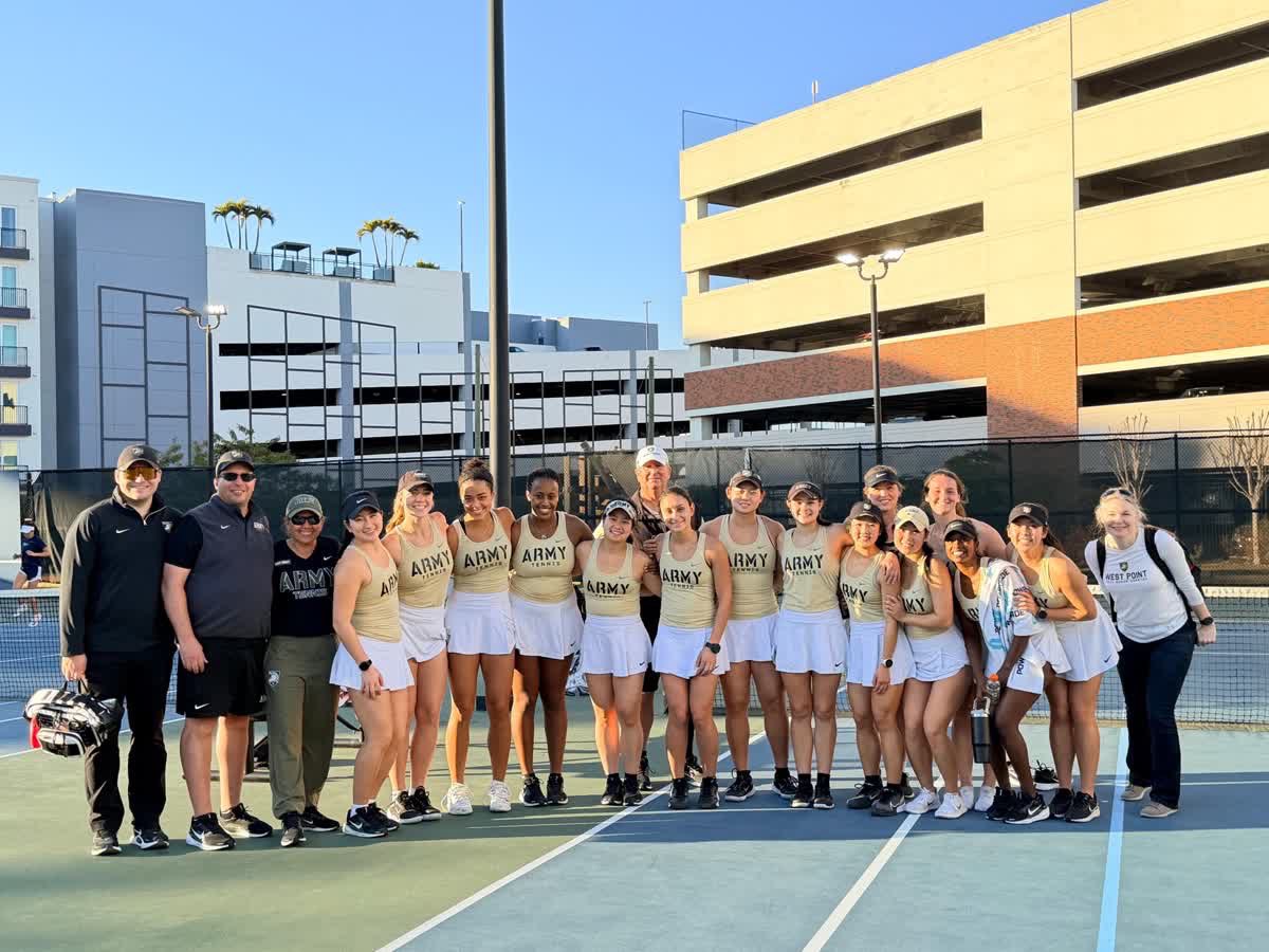 Army West Point women’s tennis players pose with their coaching and support staff on an outdoor court after a match.