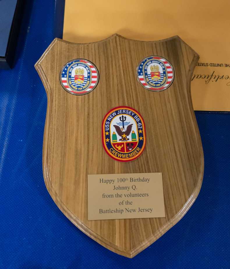 A wooden commemorative plaque honoring Johnny Q’s 100th birthday from Battleship New Jersey volunteers sits on a table aboard the museum ship in Camden, N.J.